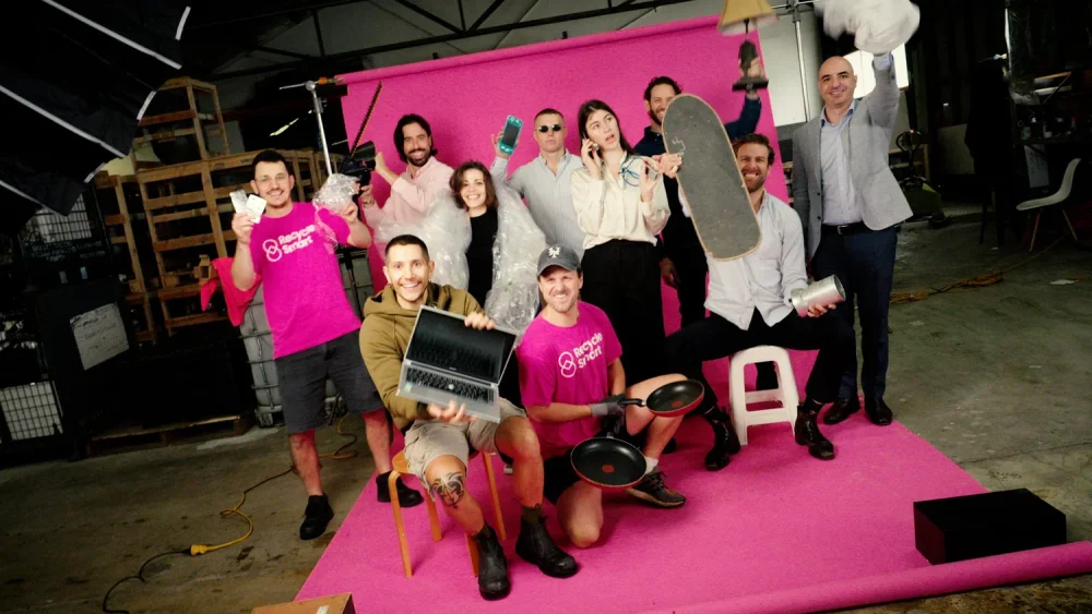 The ReSmart team posing with recyclable items on a pink studio backdrop