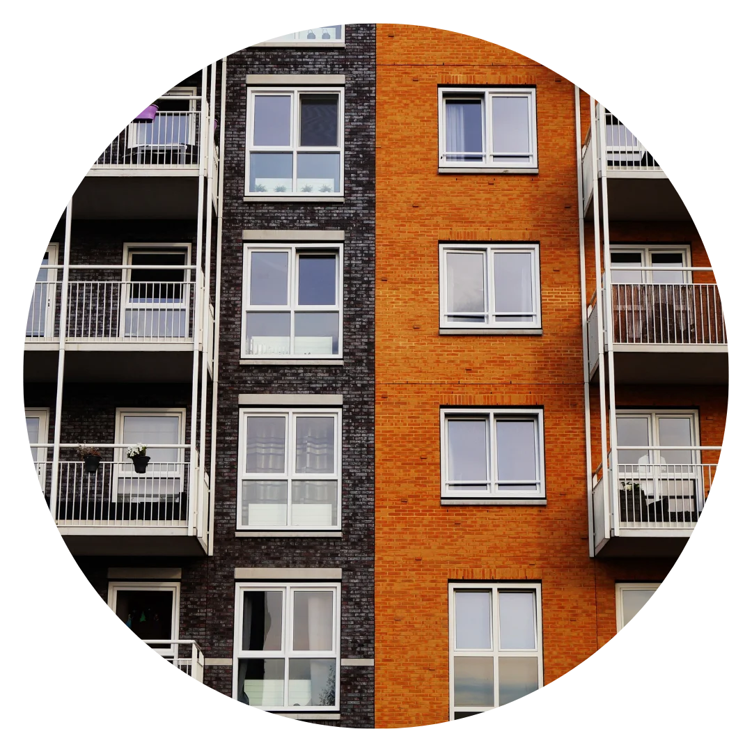 Close-up of two apartment buildings with contrasting brick exteriors, one dark brown and one orange, featuring multiple white-framed windows and balconies with metal railings.