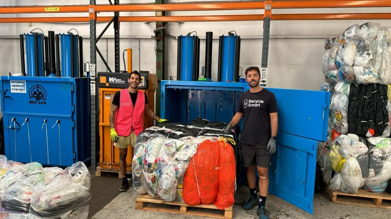 Two men in a recycling facility beside large bundles of baled plastic