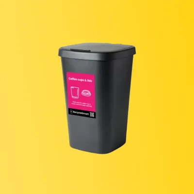 Black bin with pink label for coffee cups and lids on a yellow background