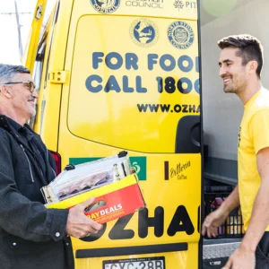 OzHarvest volunteer handing over a box beside a yellow OzHarvest van
