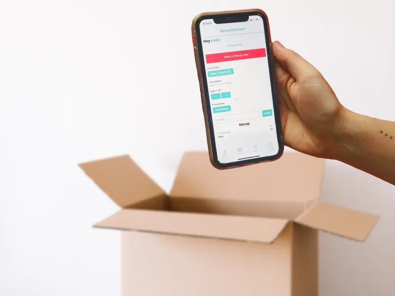 A hand holding a phone with the booking app above an open cardboard box