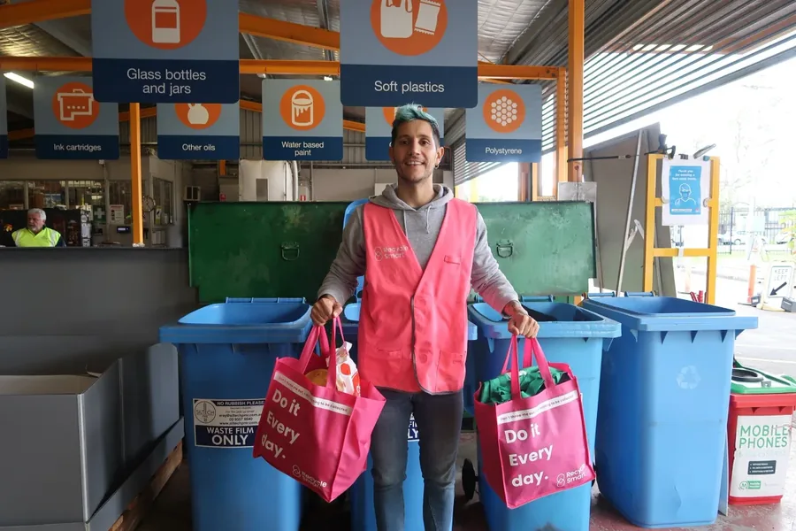 ReSmart team member in a pink vest holding bags beside recycling bins