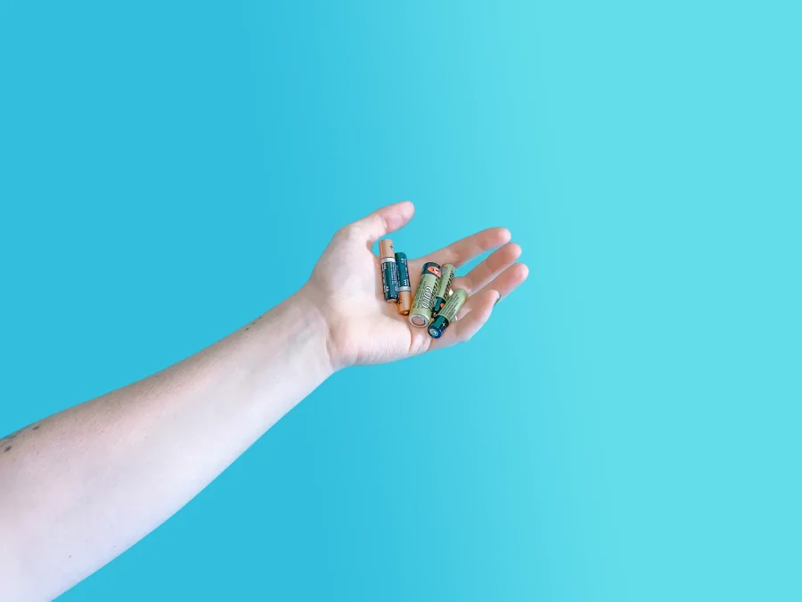 Hand holding several used batteries against a light blue background