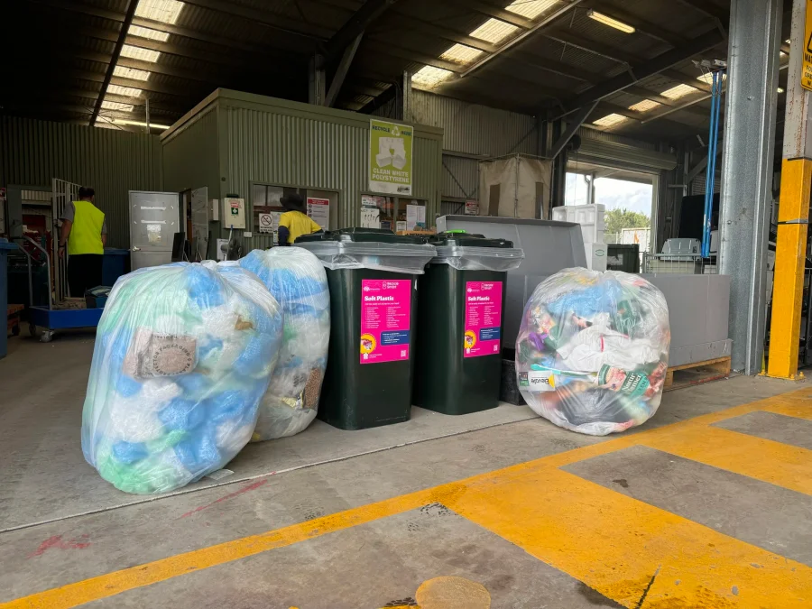 Bags of crushed plastic and three recycling bins in a warehouse