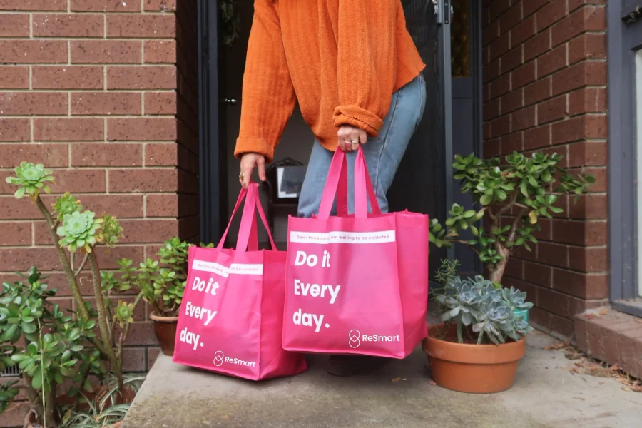 Person on a porch holding two pink ReSmart reusable bags