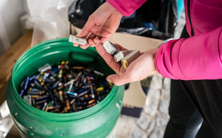 Person in a pink jacket dropping batteries into a large green container