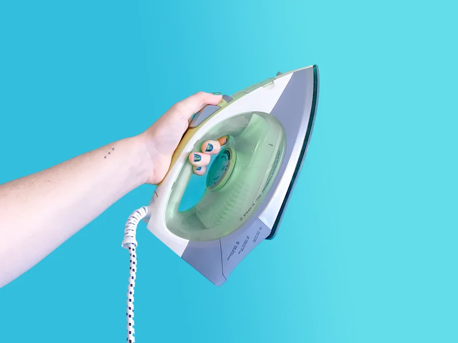 Hand holding a steam iron against a blue background