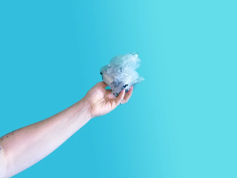Hand holding crumpled soft plastic against a blue background