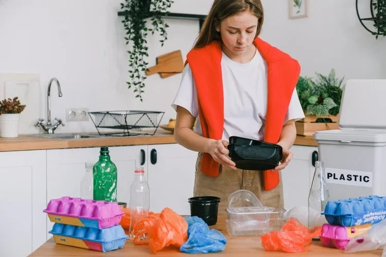 A young woman at a kitchen table preparing plastic bottles and bags for recycling