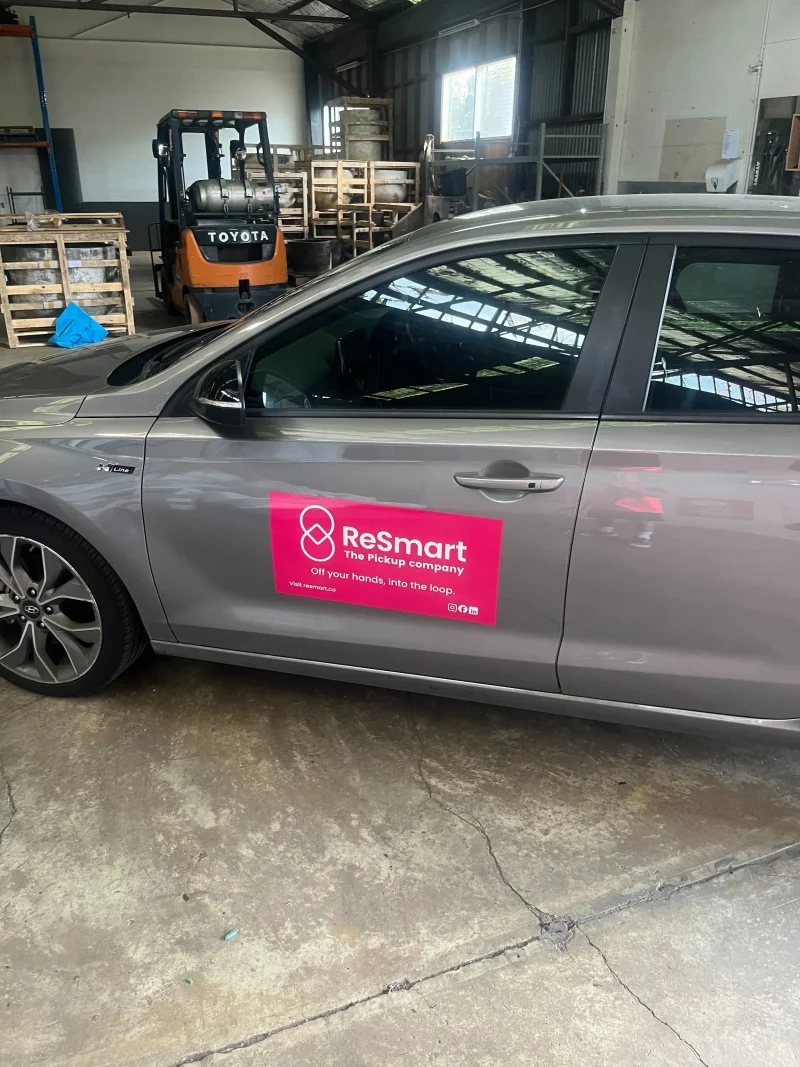 Grey car with a pink ReSmart sign on its door, parked in a warehouse