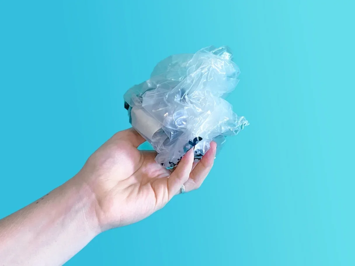 A hand holding a crumpled plastic bag against a solid light blue background.