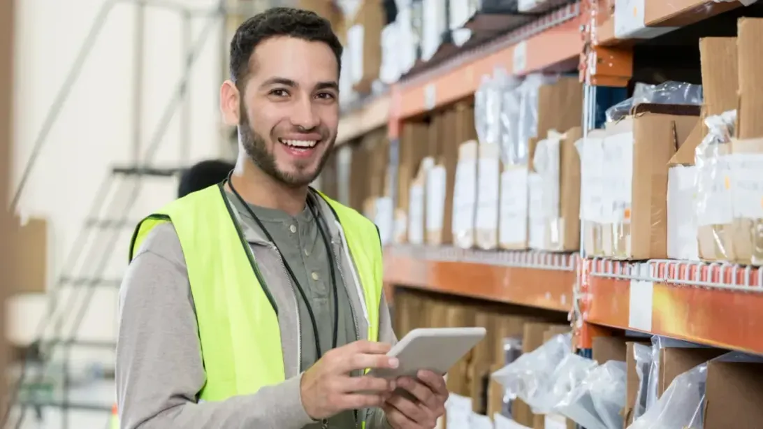 Smiling warehouse worker in a hi-vis vest holding a tablet