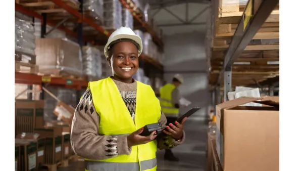 Warehouse worker in a hard hat and hi-vis vest holding a tablet