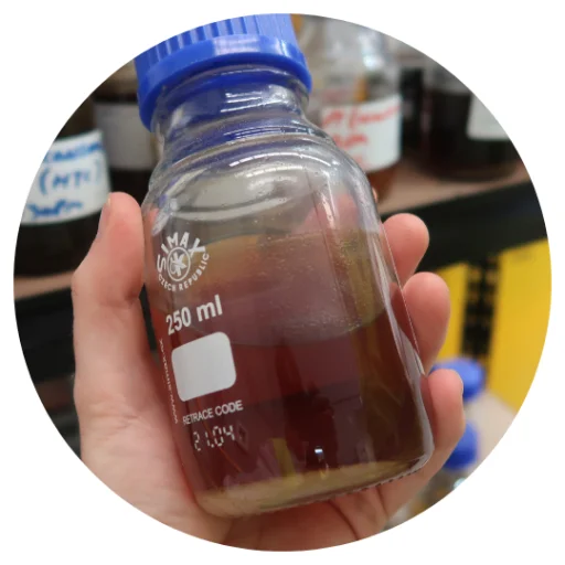 A hand holding a glass bottle of dark feedstock oil made from soft plastics