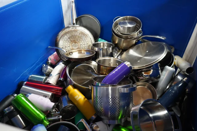 A blue crate full of sorted metal cookware and drink bottles