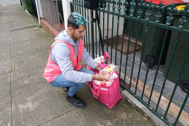 A ReSmart driver crouching to collect a pink pickup bag at a front gate